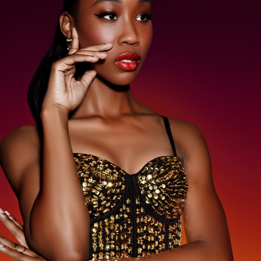 Image of model with deep-toned skin wearing High-Pigment Gloss in Coral by Beauty For Certain.